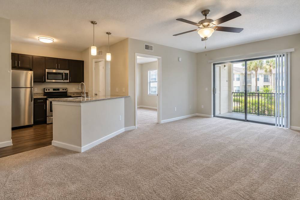 Vacant apartment living area and kitchen with clean carpet and a balcony door