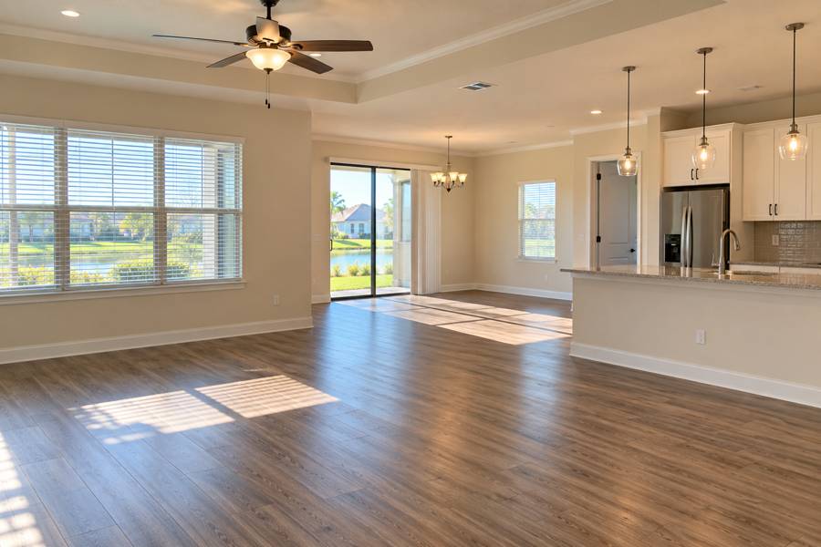 Empty open-plan home with wood floors, sunlit windows and a kitchen